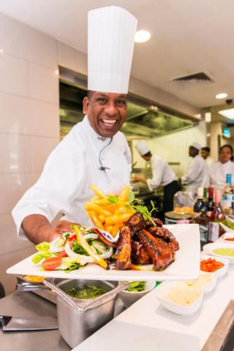 a chef standing in a kitchen with a plate of food at ONOMO Hotel Cape Town – Inn On The Square in Cape Town