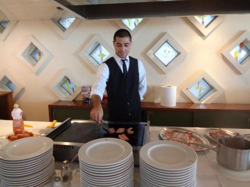 Un uomo in piedi in una cucina che prepara il cibo di Hotel Ambasciatori Palace a Lido di Jesolo