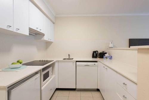 a white kitchen with white cabinets and a sink at Grande Esplanade Studio in Sydney