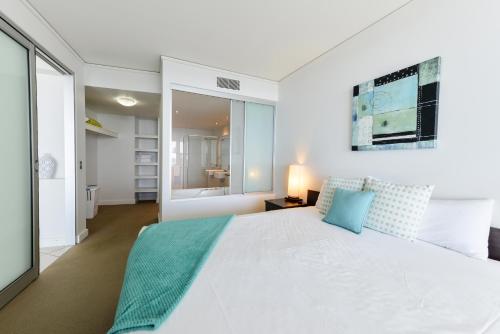 a white bedroom with a large bed and a bathroom at C Bargara Resort in Bargara