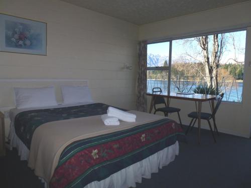 a hotel room with a bed, chair, table and window at Lakeside Motel in Queenstown