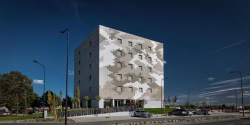 a tall building with cars parked in a parking lot at Hotel The Cube in Fidenza