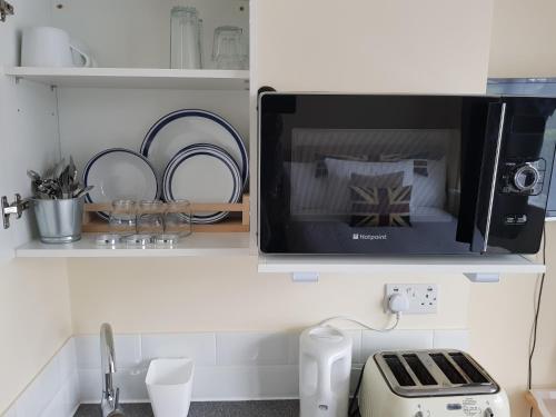 a microwave oven above a kitchen counter with dishes at Kathleen House Plus in Enfield