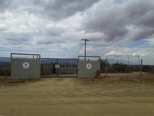 a gate in a dirt field with a cloudy sky at Natures Rest Lapa in Oudtshoorn