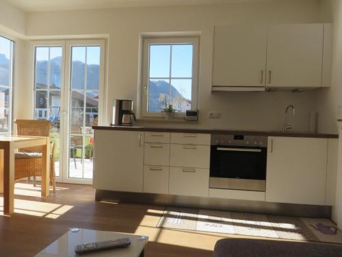 a kitchen with white cabinets and a table and windows at Ferienwohnung am Golfplatz in Grassau