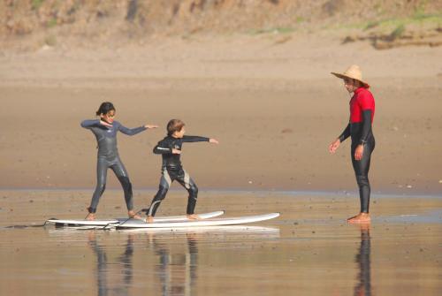 three people standing on a surfboard on the beach at Aftas Trip in Mirleft