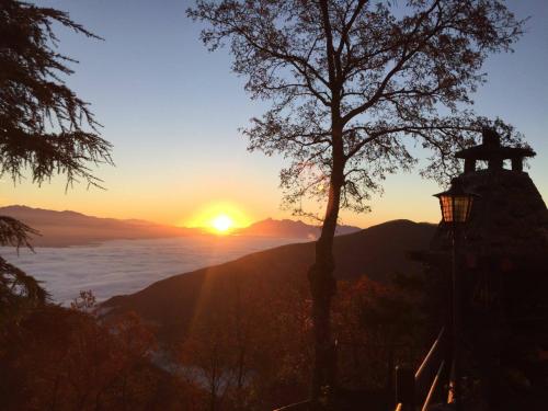 a sunset over the ocean with a lighthouse and a tree at Locanda Il Rustichello in Mulazzo