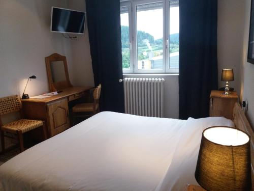 a bedroom with a bed and a desk and a window at Hôtel De La Paix in Gérardmer