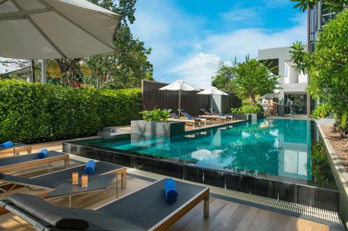 a swimming pool with chairs and an umbrella at Somerset Ekamai Bangkok in Bangkok