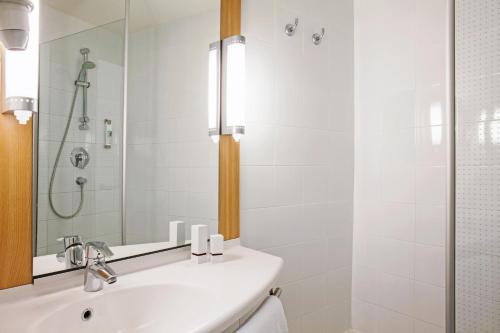 a white bathroom with a sink and a shower at Hotel ibis Porto Sul Europarque in Santa Maria Da Feira