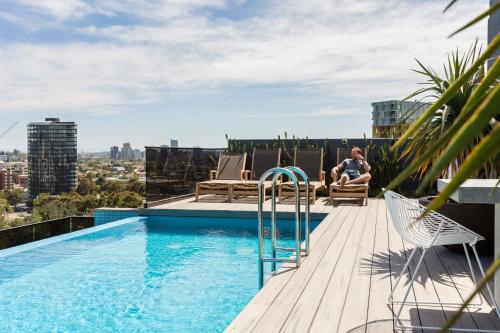 a man sitting on a chair next to a swimming pool at COMPLETE HOST Park View St Kilda in Melbourne