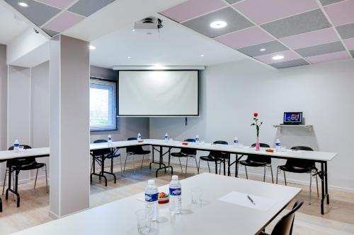 a conference room with tables and chairs and a screen at Hôtel & Résidence Octel in Portet-sur-Garonne