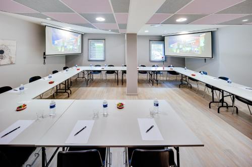 a conference room with tables and chairs and projection screens at Hôtel & Résidence Octel in Portet-sur-Garonne