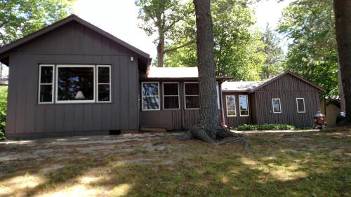 a small house with a tree in a yard at Log Cottage on Blue Lake in Kalkaska