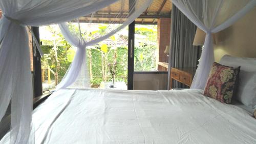 a bedroom with a white bed with a large window at Griya Sriwedari in Ubud