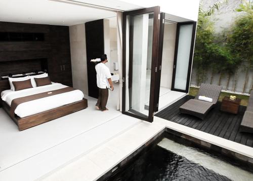 a man in a bedroom with a bed and a pool at eqUILIBRIA Seminyak in Seminyak