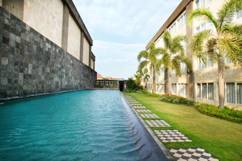 ASTON Denpasar Hotel & Convention في دينباسار: مسبح بجانب مبنى فيه نخيل