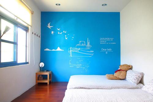 a teddy bear sitting on a bed with a blue wall at Ecotourism skim month B & B in Xiaoliuqiu