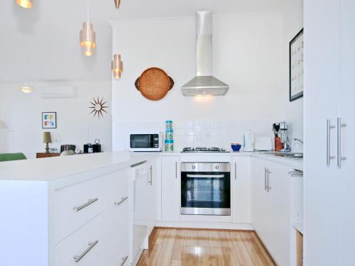 a white kitchen with white appliances and a wooden floor at Kiltevna - Maslin Beach - C21 SouthCoast Holidays in Maslin Beach