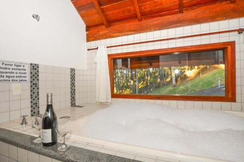 a bath tub with a bottle of wine and a window at Pousada Ágape in Monte Verde