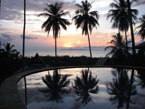 a reflection of palm trees in a pool with a sunset at Villa Liu in Nathon