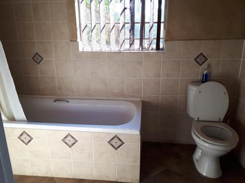 a bathroom with a tub and a toilet and a window at Vivian's Cottage in Pretoria