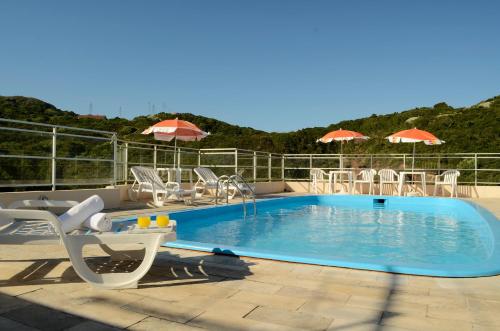 uma piscina com cadeiras, mesas e guarda-sóis em Joaquina Beach Hotel em Florianópolis