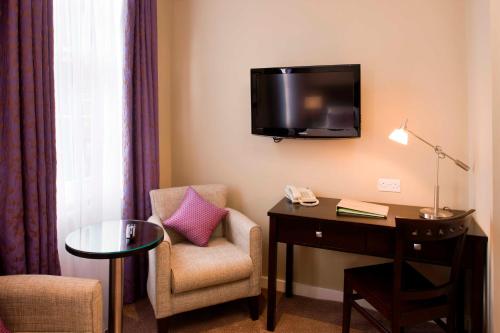 a hotel room with a chair and a desk and a tv at Berjaya Eden Park London Hotel in London