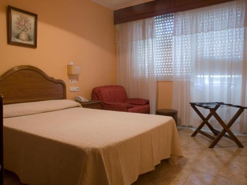 a bedroom with a bed and a chair and a window at Hotel Marcial in Narón