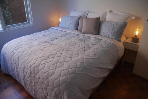 un grande letto con piumone e cuscini bianchi di Balcony Retreat Apartment by Ready Set Host a Melbourne