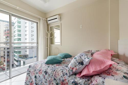 1 dormitorio con cama con almohadas y ventana en Apartamento Coral - 1 quadra do Mar, en Balneário Camboriú