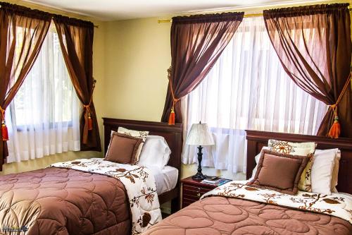- une chambre avec 2 lits et des fenêtres avec des rideaux dans l'établissement Hostal Saint Mary´s Tababela, à Tababela