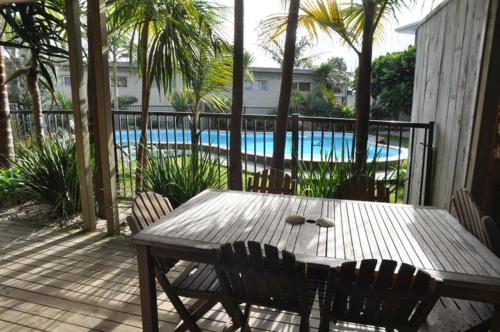 una mesa de madera y sillas en un patio con piscina en Waipu Cove Resort, en Waipu