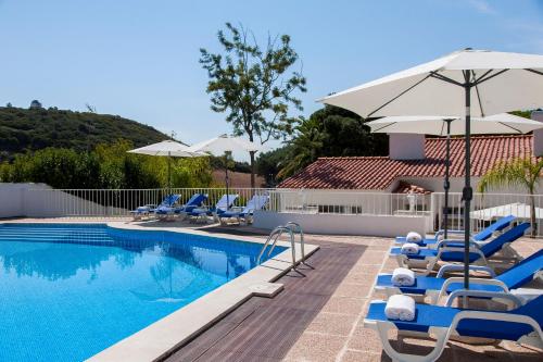 a swimming pool with lounge chairs and an umbrella at Villa Branca do Castelo in Sesimbra
