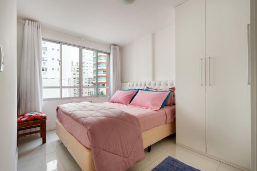 1 dormitorio con cama con sábanas rosas y ventana en Apto 2 quartos, 1 quadra do Mar/Shop. Atlantico, en Balneário Camboriú