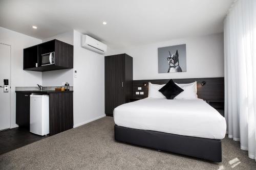 a bedroom with a large white bed and a kitchen at The Metrotel in New Plymouth