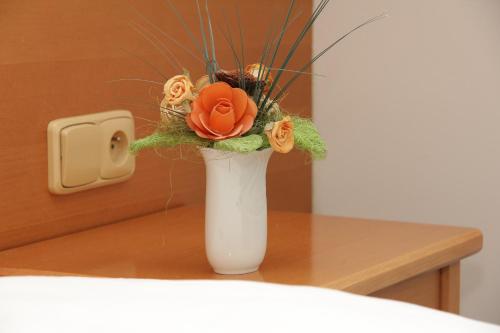 a white vase with orange roses in it on a table at Penzion Budvarka in Hodonín
