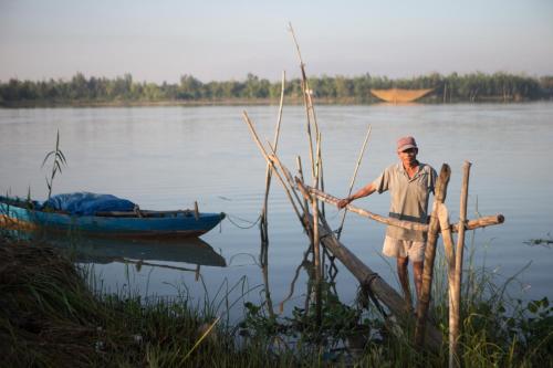 a man is standing in the water with a boat at Riverside Hamlet Homestay & Villa in Hoi An