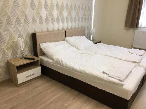 a bed with white sheets and a night stand with a lamp at Kristály apartmanok in Kisvárda