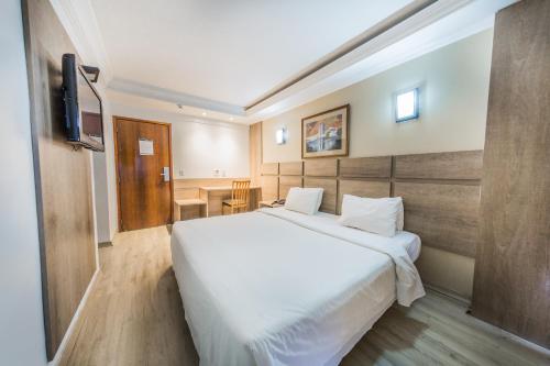 um quarto com uma grande cama branca e uma televisão em Phenícia Bittar Hotel em Brasília