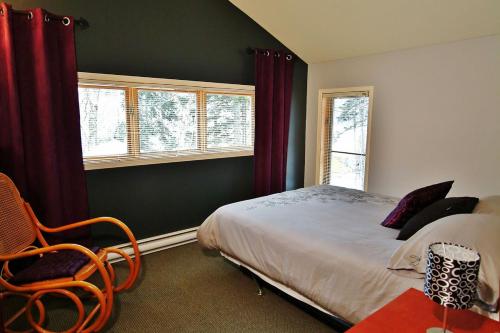 a bedroom with a bed and a chair and windows at Chalets Alpins - 01 Chemin Alpin in Stoneham