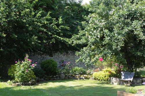 un jardín con una pared de piedra, árboles y flores en La Poussiniere, en Auvers-Saint-Georges