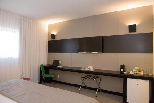 a bedroom with a bed and a desk with a green chair at Wyndham Garden Ribeirão Preto Convention in Ribeirão Preto