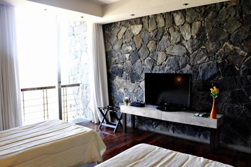 a bedroom with a stone wall with a television at Tres Pircas Hotel & Spa in Huerta Grande