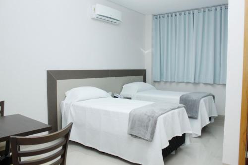 a bedroom with two beds with white sheets and a table at Hotel Cadori in Paiçandu