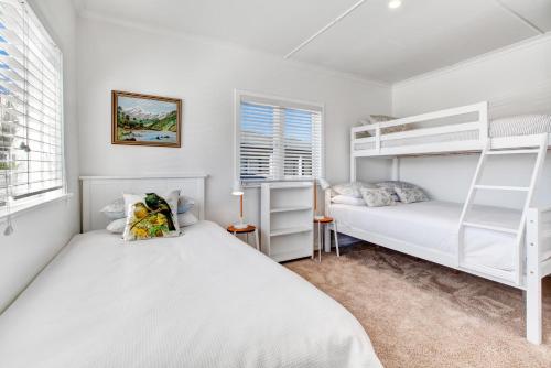 two beds in a bedroom with two bunk beds at The Little Blue Bach in Oneroa Village by Waiheke Unlimited in Oneroa