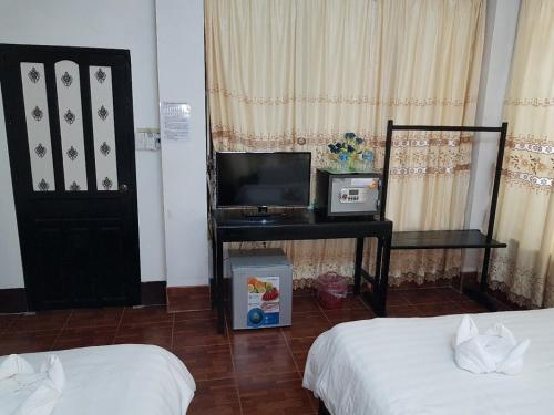 a room with two beds and a desk with a television at Maylay Guesthouse in Vang Vieng
