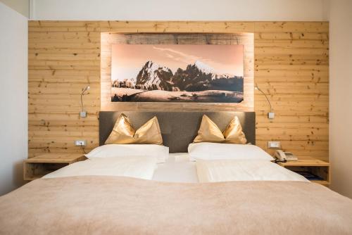 a bedroom with a large bed with white sheets and gold pillows at Hotel Kranebitt B&B in Bressanone