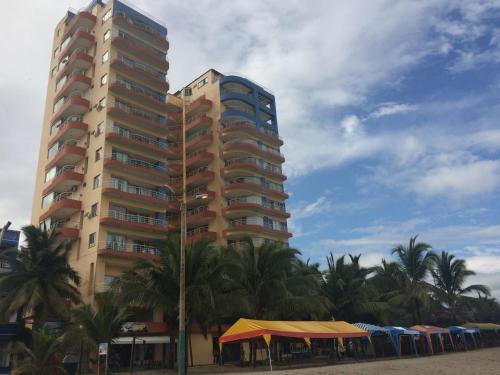 un edificio alto en la playa con palmeras y sombrillas en Apartamento en Atacames con vista al mar en Atacames