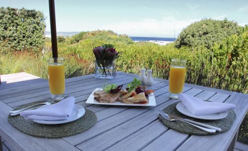 a table with a plate of food and two glasses of orange juice at Mosselberg on Grotto Beach in Hermanus